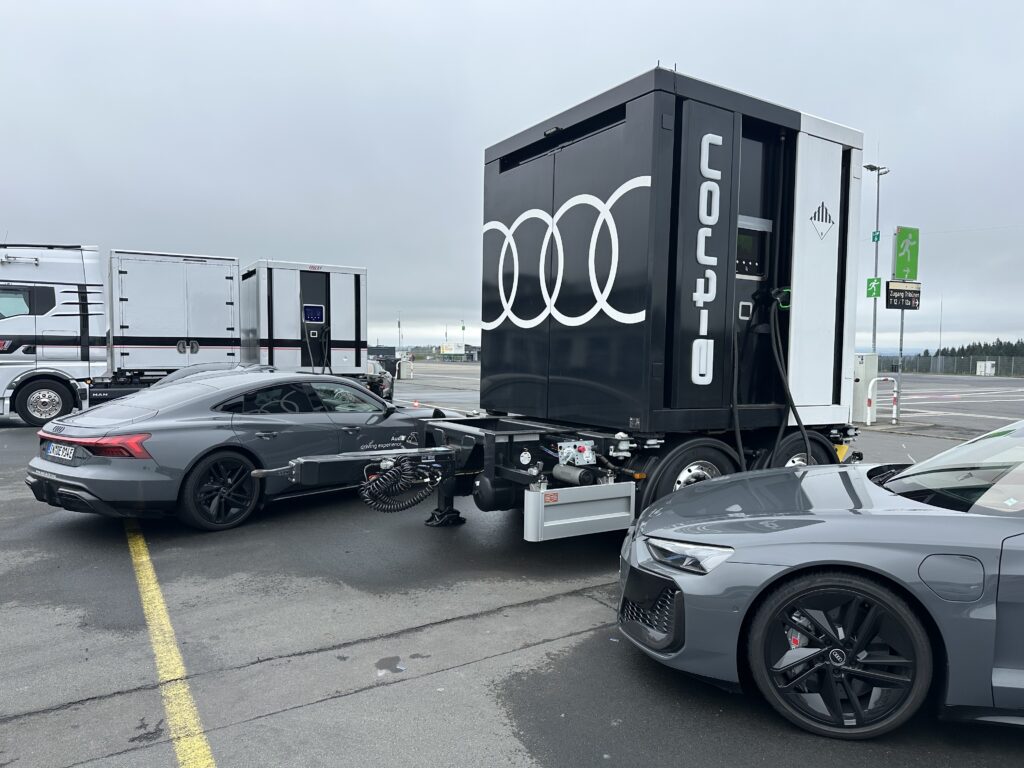 Justsiks koki Audi driving experiencen Nürburgringillä: märkää rataa ja unohtumaton ajopäivä Harmaita Audi e-tron GT -autoja ja siirrettäviä Audi-latausyksiköitä Nürburgringin varikolla.